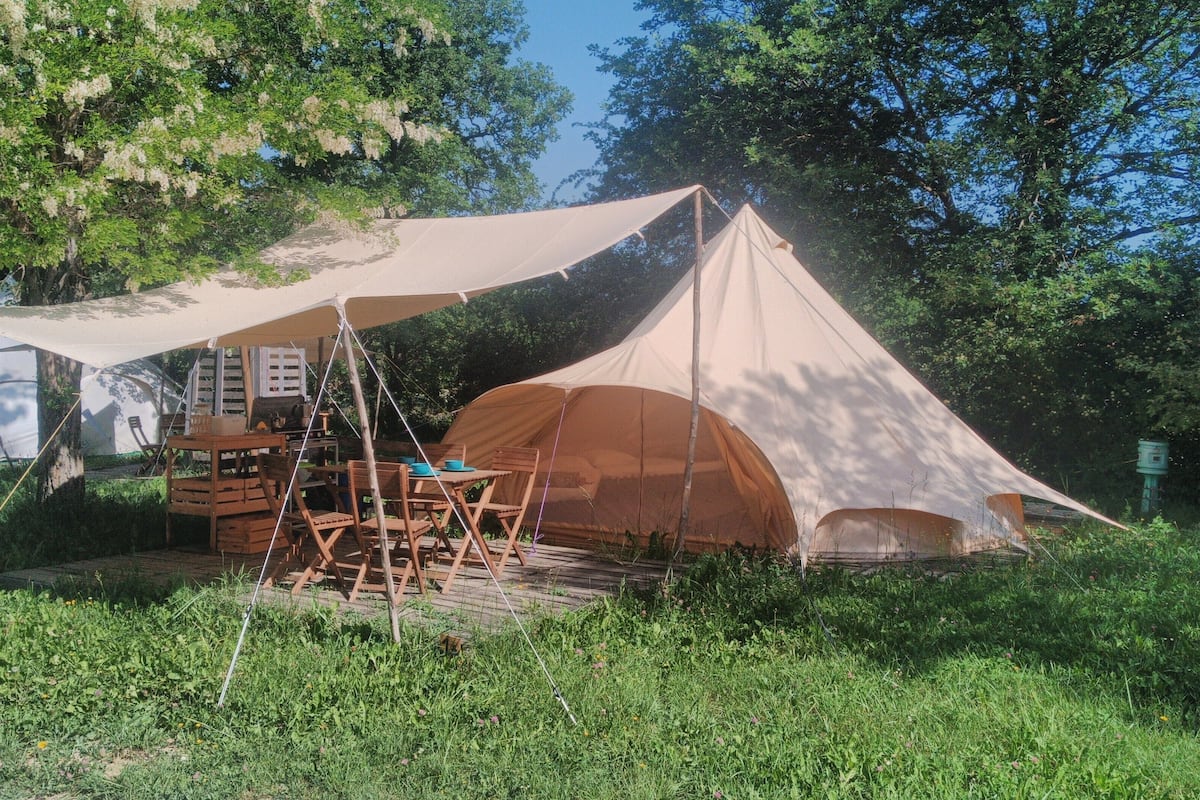 Una carpa con una mesa y sillas instaladas en un área verde rodeada de árboles.