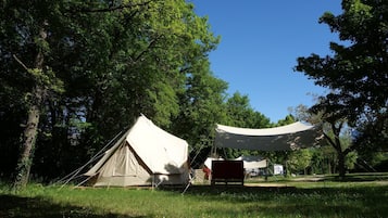 A tented campsite with a large canopy and a smaller tent, surrounded by trees and grassy area.