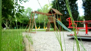 Een speeltuin met schommels en een glijbaan, omringd door gras en bomen.