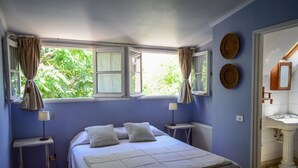 Een slaapkamer met een bed, twee nachtkastjes, een raam met gordijnen, en een badkamer met een wastafel en spiegel.