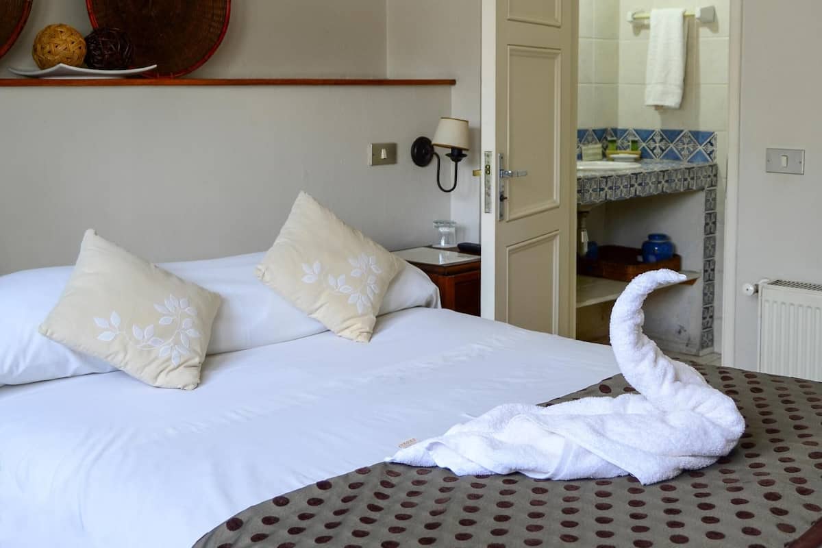 Habitación de hotel con cama, baño visible a través de una puerta abierta y estante empotrado con platos decorativos.