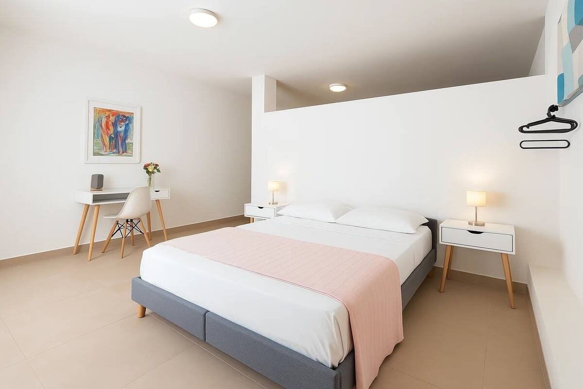 Un dormitorio con cama, mesitas de noche, escritorio y silla.