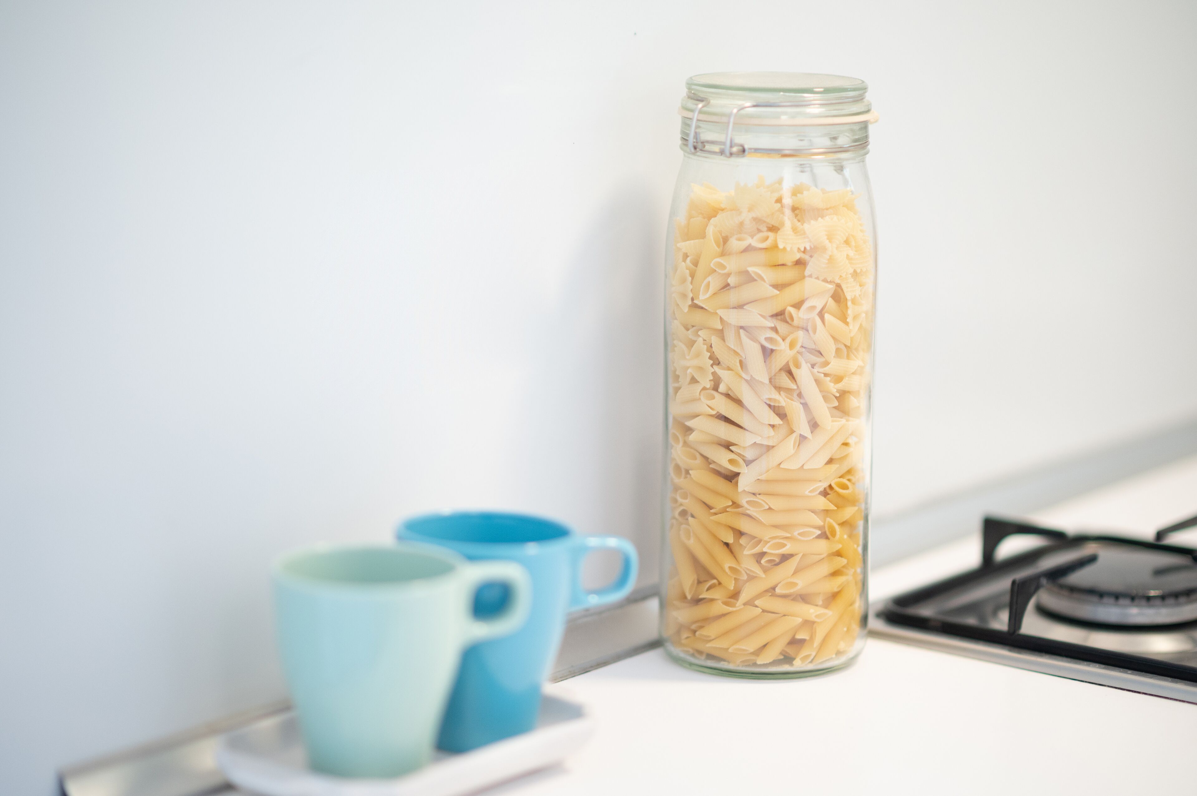 Un frasco de vidrio lleno de pasta sobre una encimera de cocina, junto a una estufa.