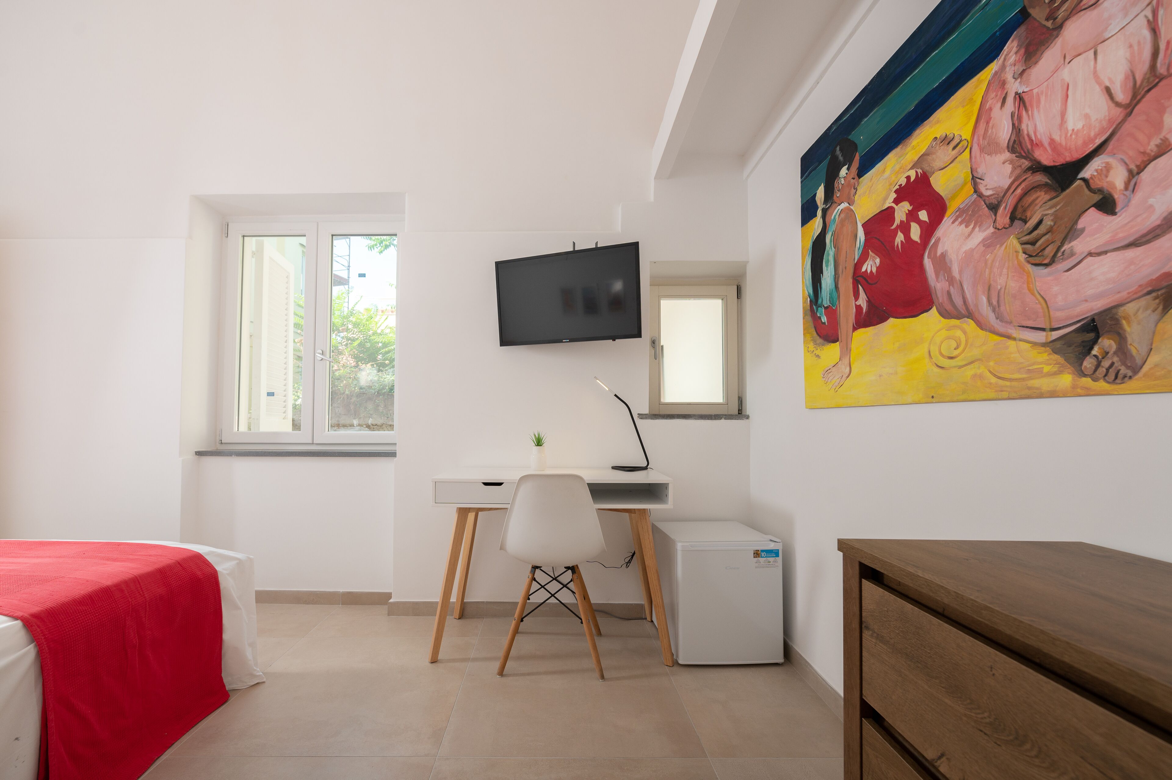 A bedroom with a bed, a desk, a chair, a TV, and a painting on the wall.
