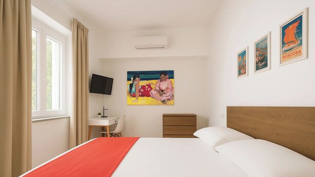 A hotel room with a bed, a desk, a chair, a TV, a nightstand, and a painting on the wall. - Gioia 13 Apartments & Rooms (Procida)