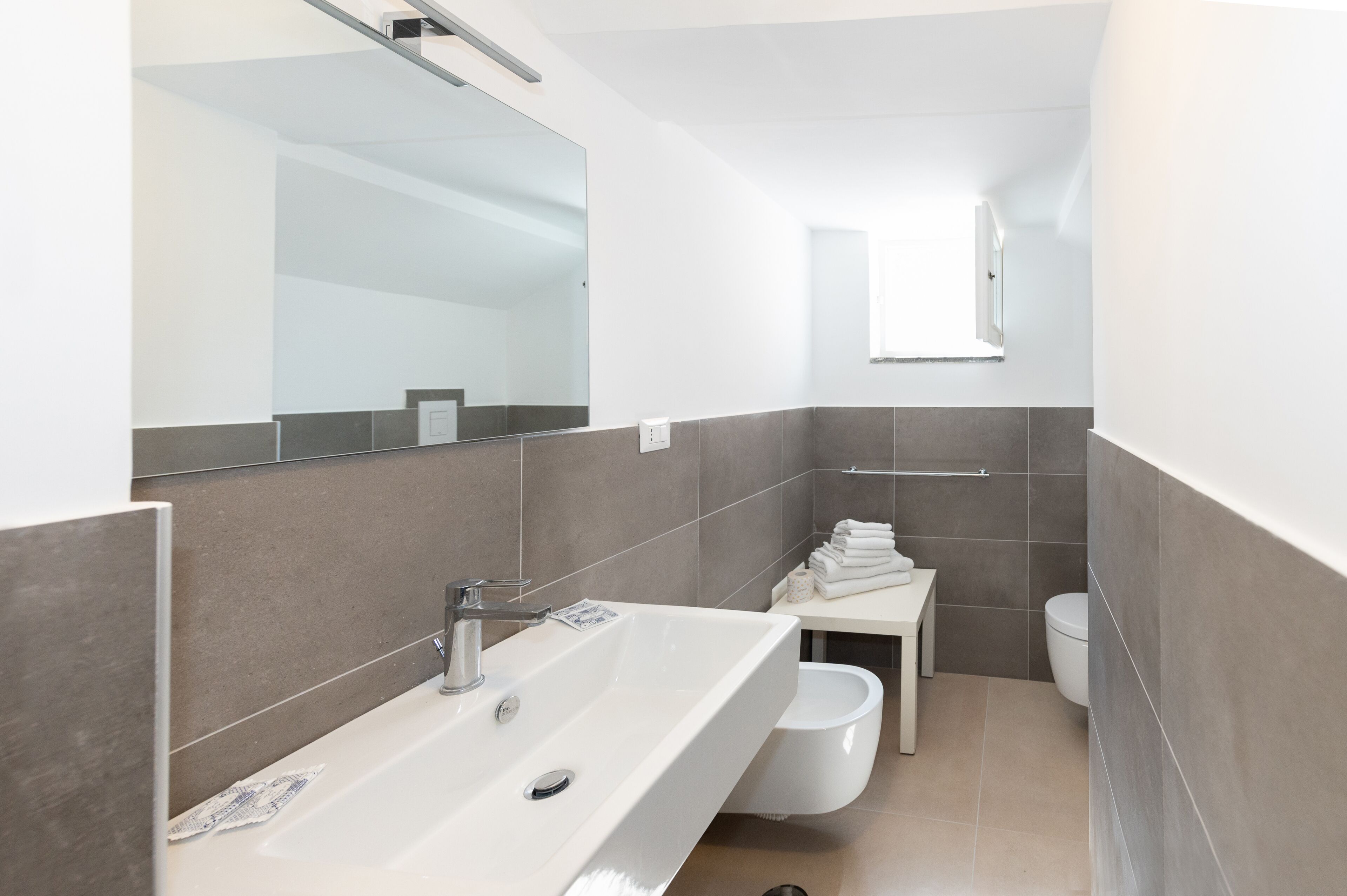 A modern bathroom with a large mirror, a white sink, and a toilet.