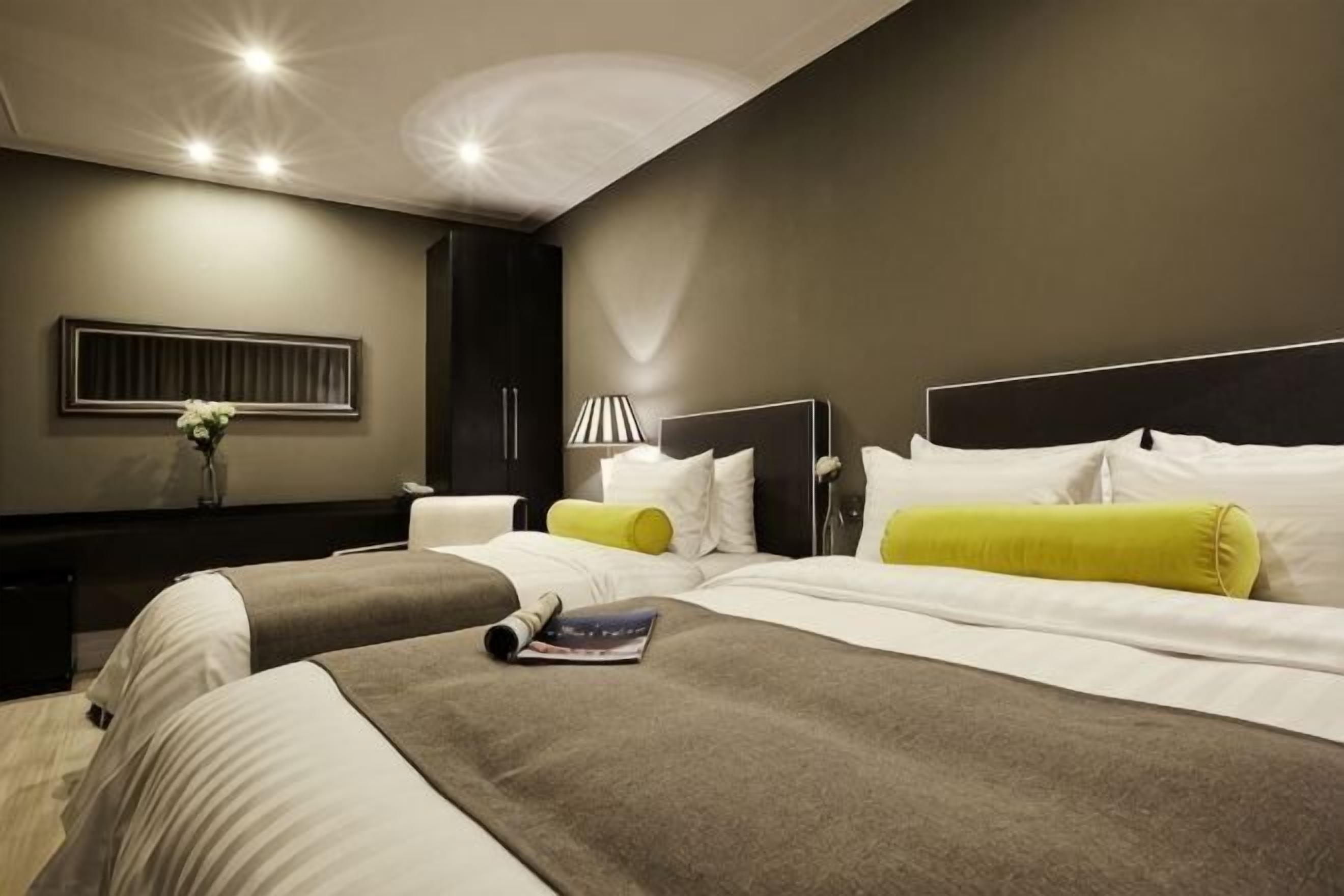 Una habitación de hotel moderna con dos camas, una mesita de noche, una lámpara y una obra de arte colgada en la pared.