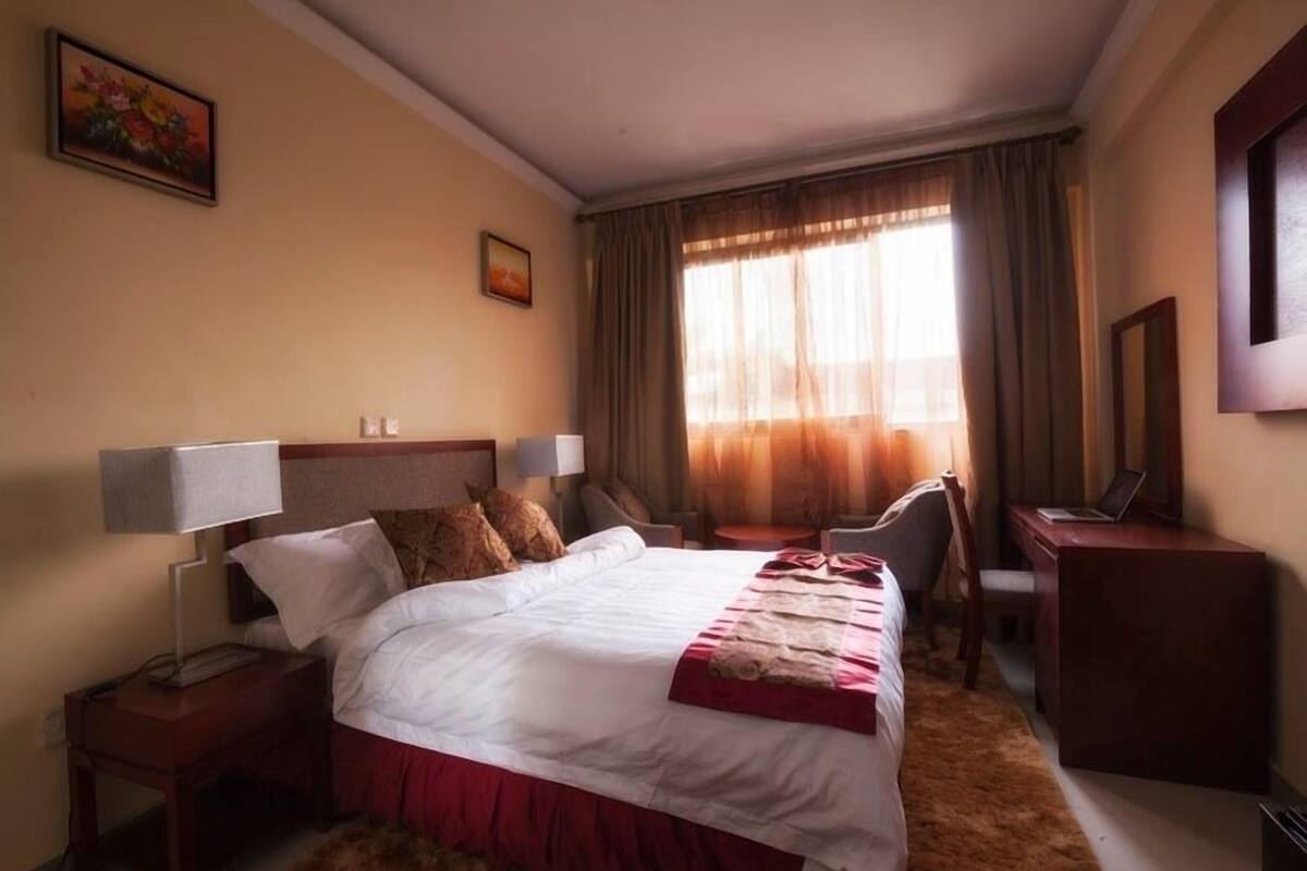 A hotel room with a large bed, a desk, a chair, and a laptop.