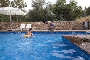 A swimming pool with a stone wall, lounge chairs, and an umbrella. - Pnai - Villa in the Galilee (Rosh Pinna)