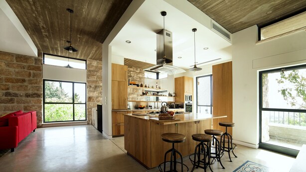 A spacious kitchen with a large island, wooden cabinets, and a red sofa. - Pnai - Villa in the Galilee (Rosh Pinna)