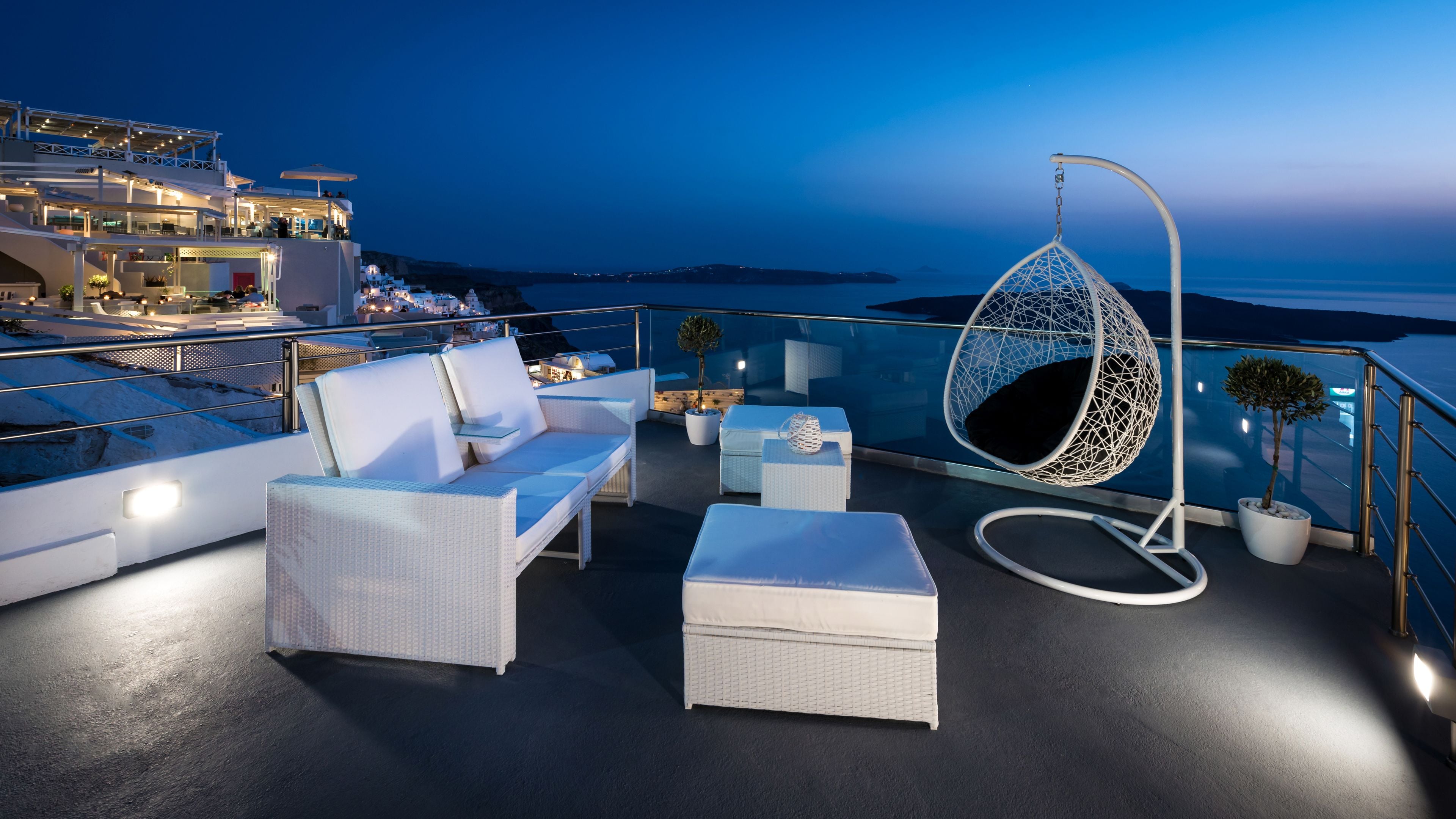 A rooftop terrace with white wicker furniture, a hanging chair, and potted plants.