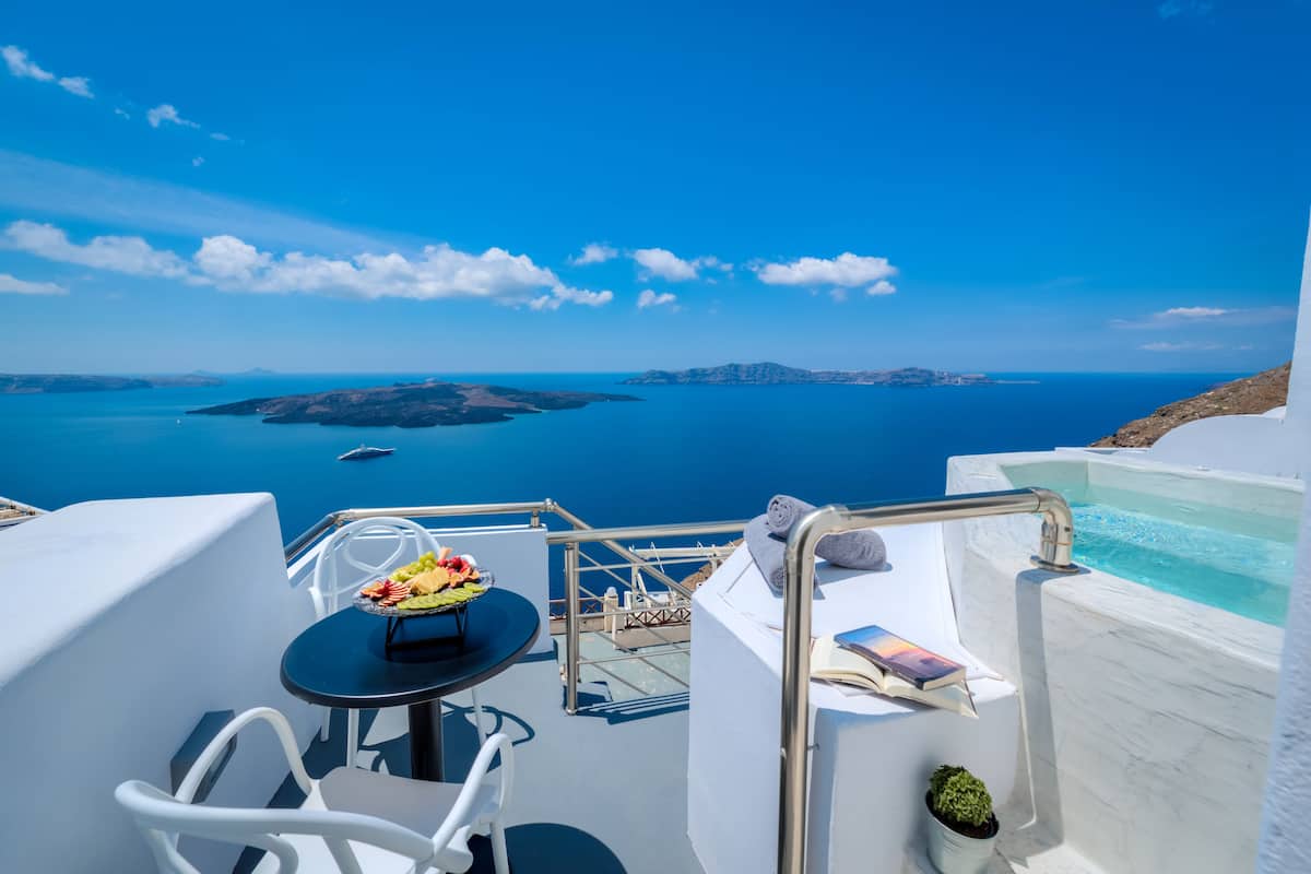 Un balcón con una mesa preparada para comer, una bañera y vistas al mar y a las islas.