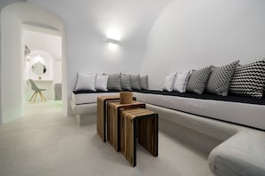 A modern, minimalist room with a white sofa, patterned cushions, and a unique wooden bench. - Modernity Suites (Santorini)