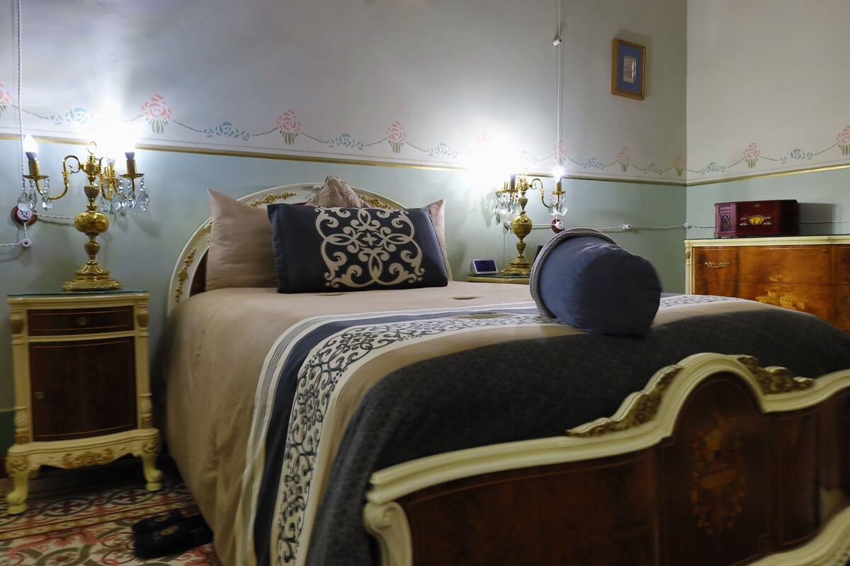 A bedroom with a bed, two nightstands, a chandelier, and a dresser.