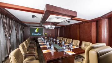 A conference room with a long table, leather chairs, water bottles, and a projector screen displaying "Eliana Hotel".