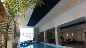 An indoor swimming pool with a ceiling that resembles a starry night sky, surrounded by potted plants and lounge chairs.