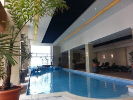 Una piscina interior con un techo que imita un cielo estrellado, rodeada de plantas en macetas y sillones de descanso.