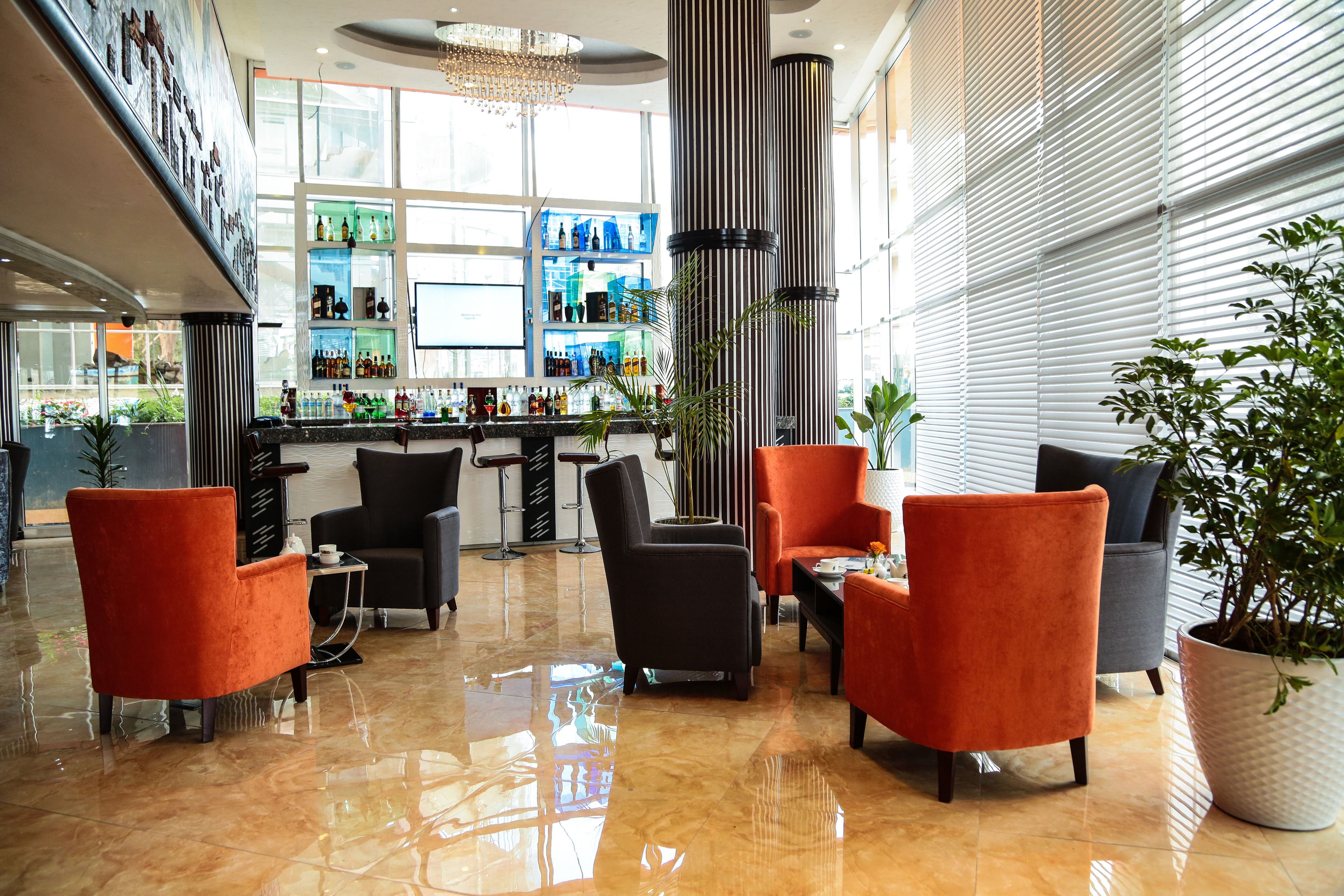 A modern bar area with a polished floor, seating with orange and black chairs, and a large potted plant.