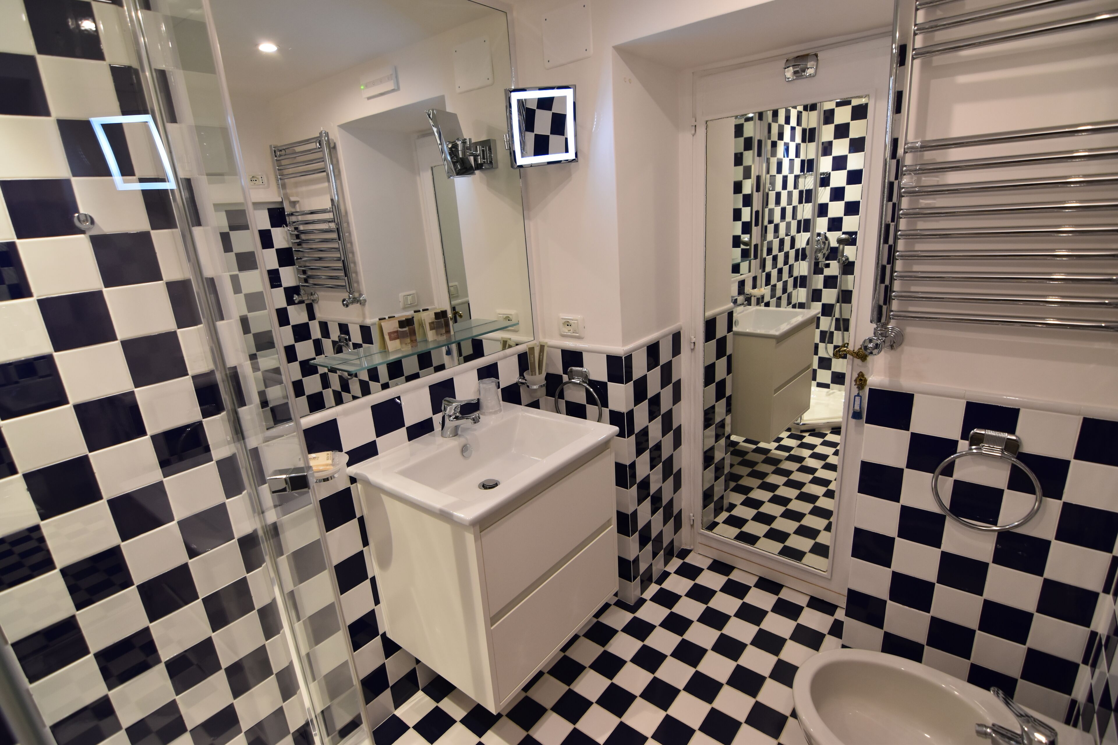 A bathroom with a checkered floor, a glass shower enclosure, a white sink, and a mirror.