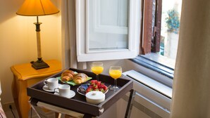 Bandeja de desayuno con cruasanes, fresas, chocolate y jugo de naranja sobre una mesa junto a una lámpara y una ventana con vistas al exterior.