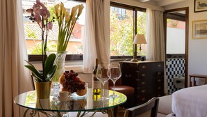 Habitación de hotel con una mesa de vidrio, un jarrón con flores, una botella de vino y un suelo a cuadros.