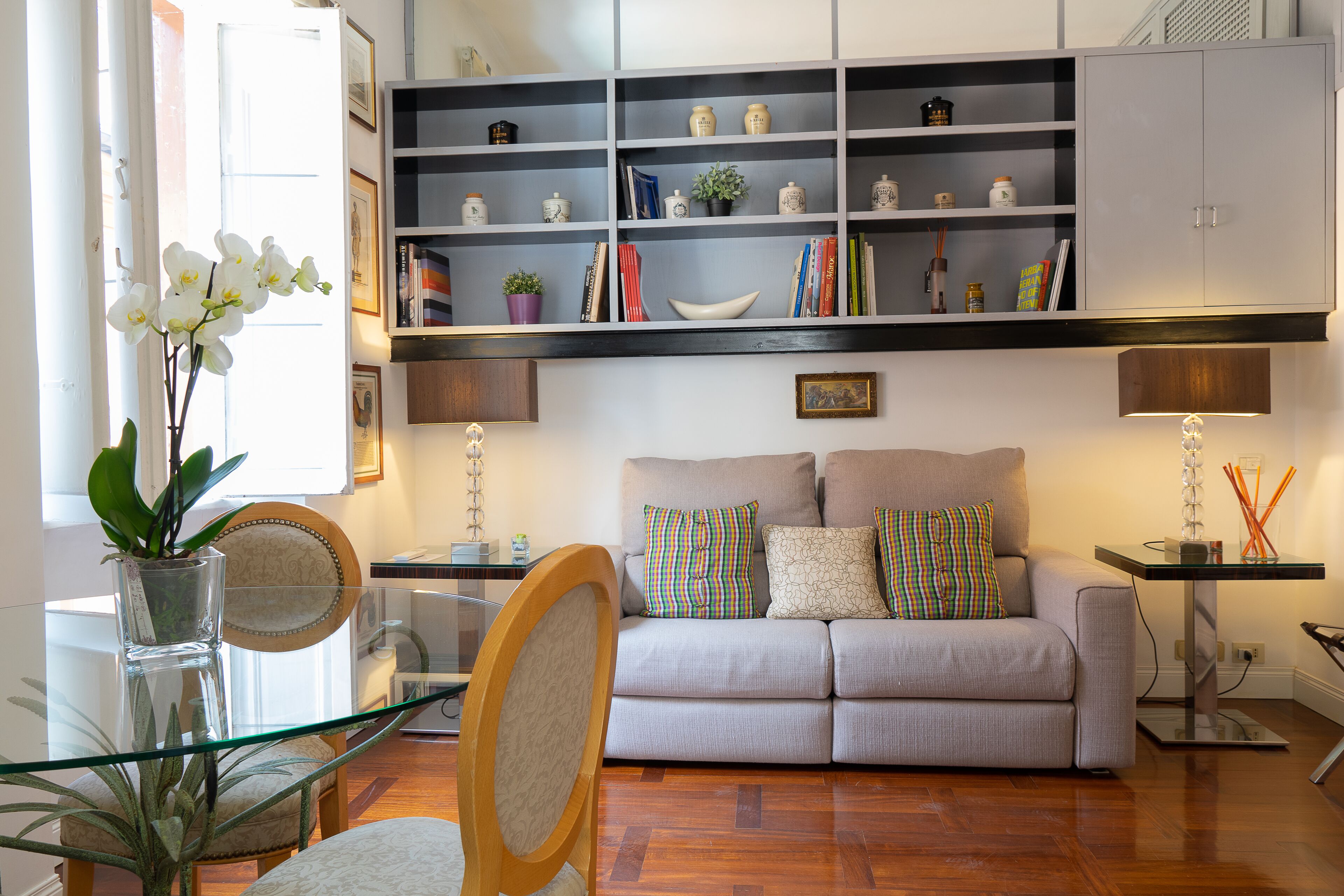 A modern living room with a sofa, glass coffee table, and a bookshelf filled with books and decorative items.