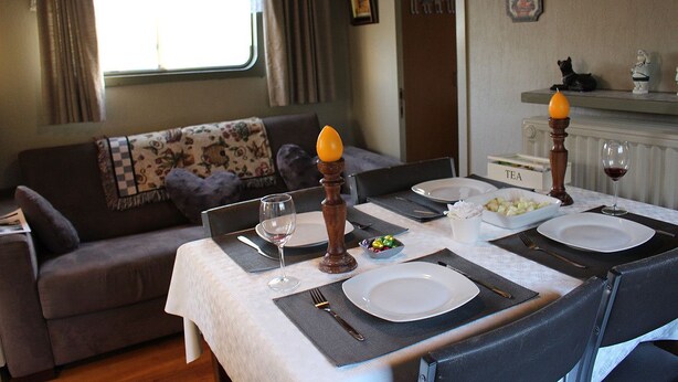 A dining area with a table set for two, a sofa, a clock, and a radiator labeled "TEA". - Spits-Lucie B&B (Izegem)