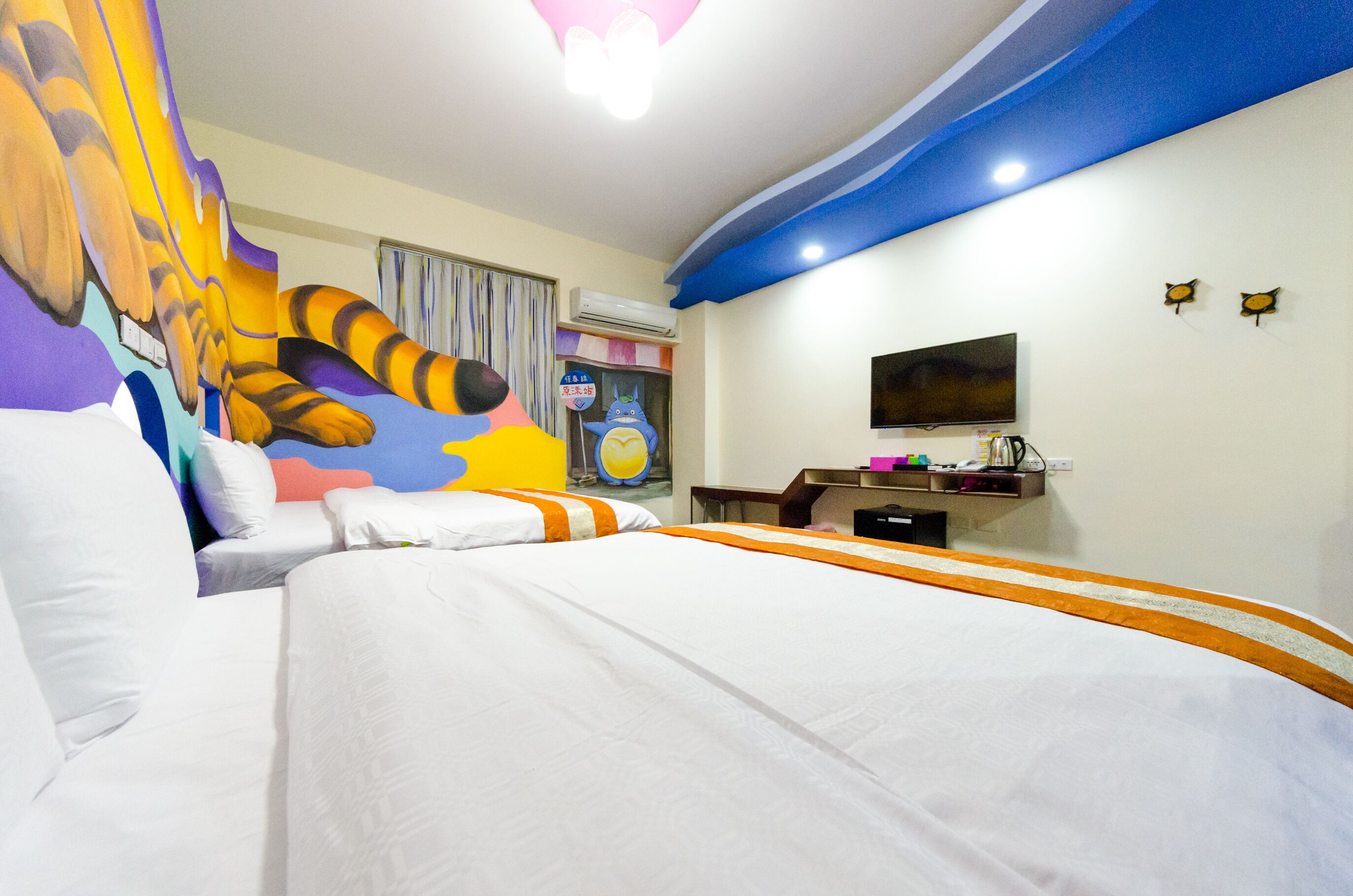 Habitación de hotel con una cama grande, un televisor, un escritorio y un mural colorido en la pared.