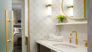 A bathroom with a marble sink, gold fixtures, a mirror, and a small shelf with toiletries.