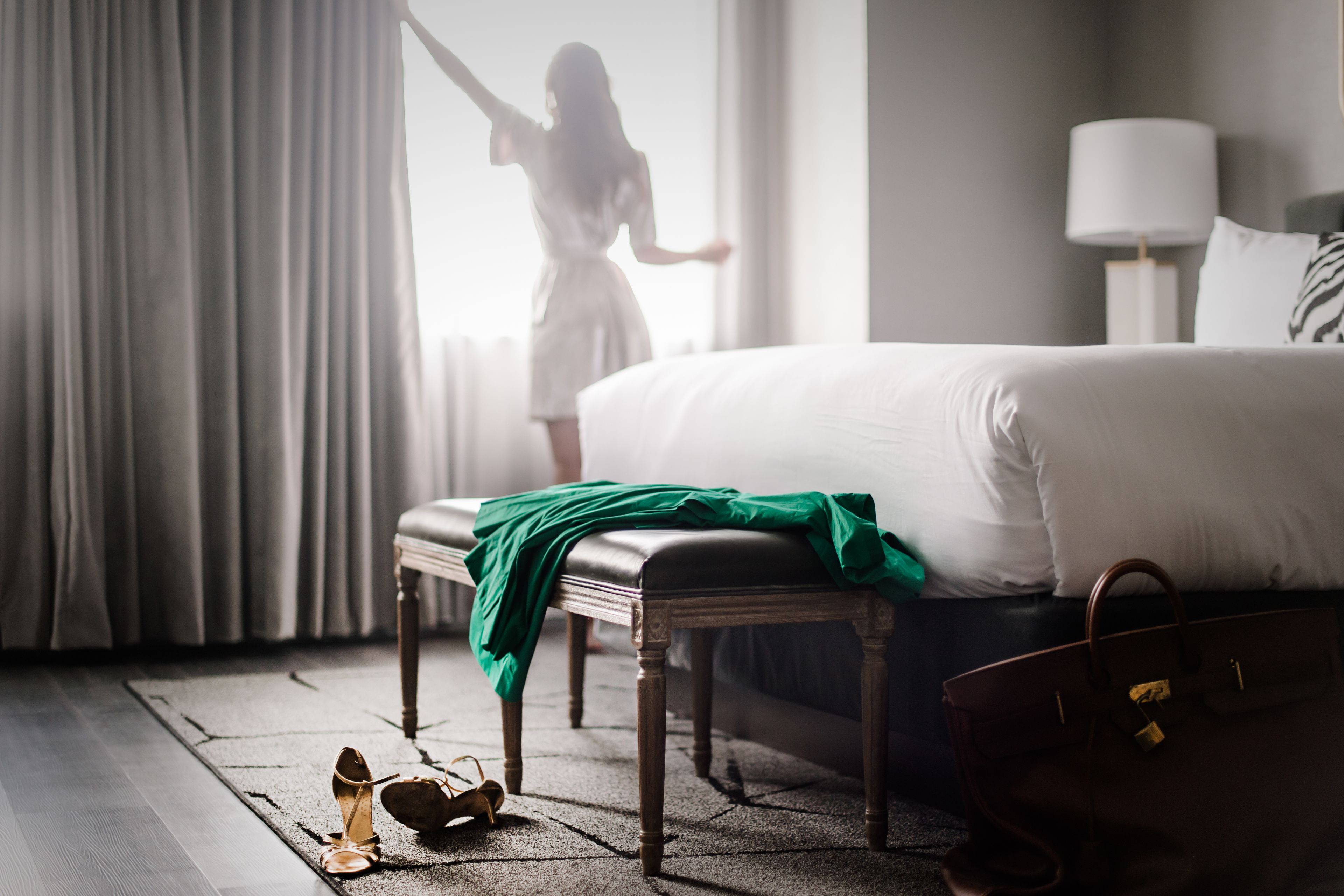 A hotel room with a large bed, a bench, a suitcase, and a pair of shoes on the floor.