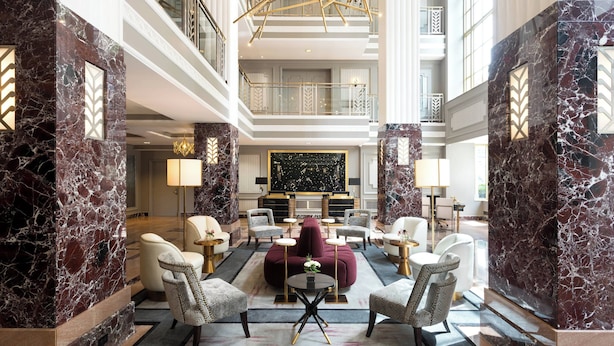 A spacious lobby with marble walls, a central seating area, and a high ceiling with a geometric light fixture. - Hotel LeVeque, Autograph Collection (Columbus)