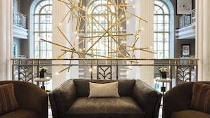 A modern lobby with a leather sofa, decorative lighting, and large windows. - Hotel LeVeque, Autograph Collection (Columbus)
