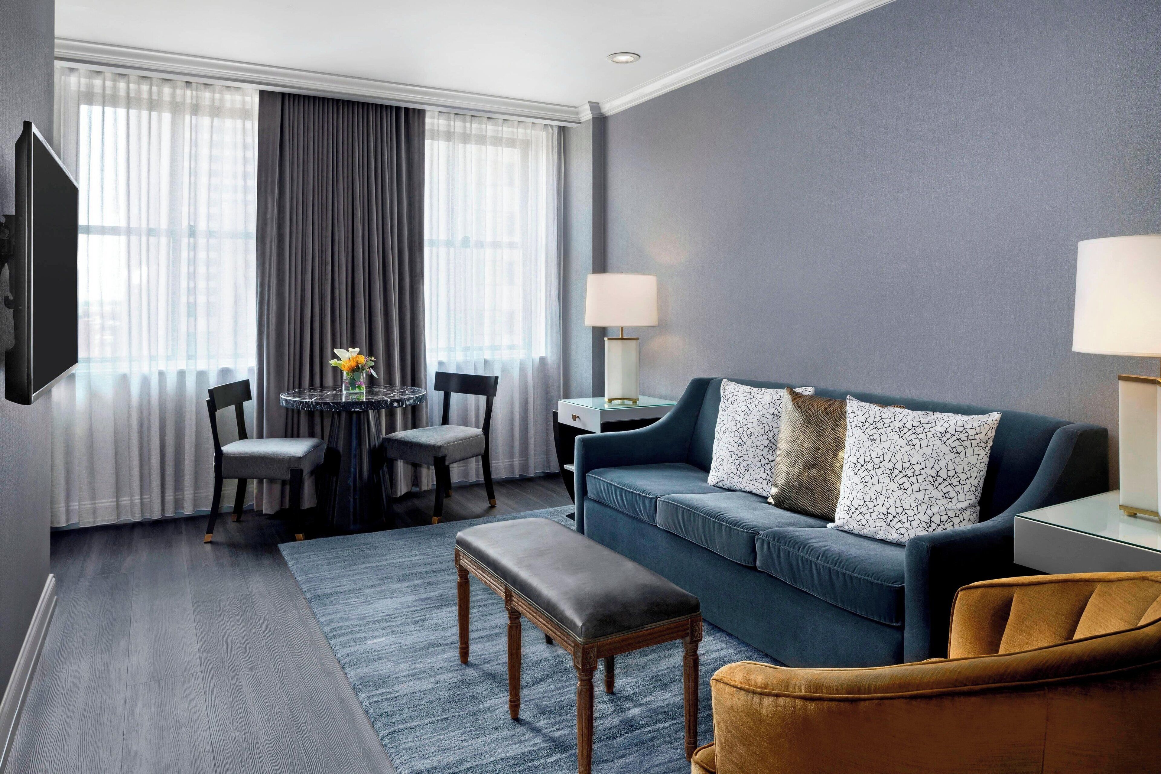 A modern living room with a blue sofa, a wooden bench, and a small round table with chairs.