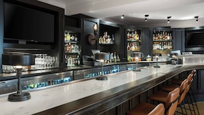 A modern bar area with a long counter, bar stools, and shelves stocked with bottles. - Hotel LeVeque, Autograph Collection (Columbus)