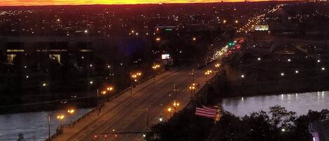 A cityscape at dusk with a river, roads, and a bridge.