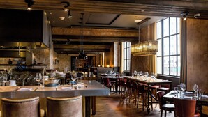 A restaurant with a long counter, multiple tables, and chairs. - Hotel LeVeque, Autograph Collection (Columbus)