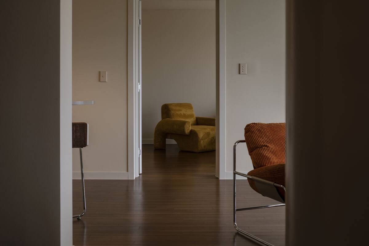 A hallway with a wooden floor, a brown chair, and a lamp.