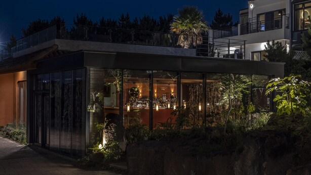 A modern building with a glass facade, a bar area, and a balcony overlooking a landscaped garden. - VILLASAGYE (Seogwipo)