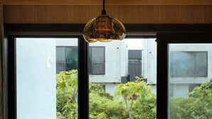 A hotel room with a bed, a table, and two chairs. There is a view of a swimming pool and greenery outside. - VILLASAGYE (Seogwipo)