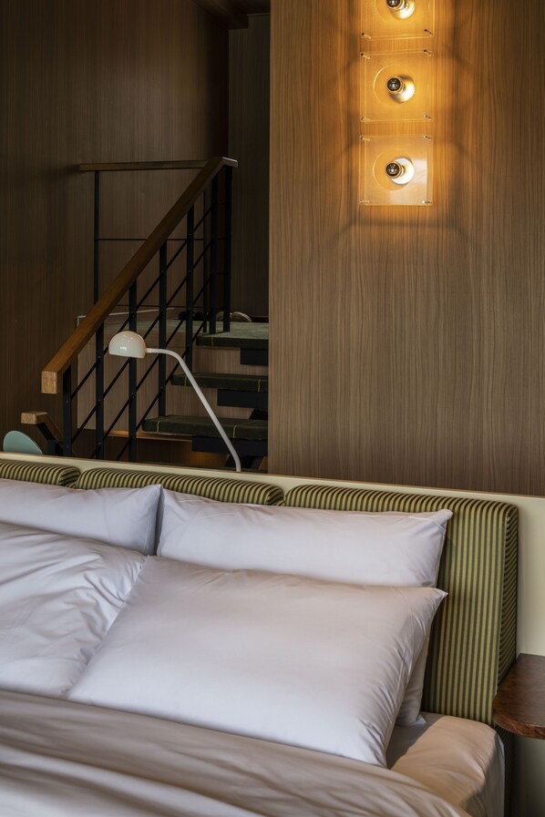 A hotel room with a wooden wall, a bed with white bedding, a nightstand, and a lamp.