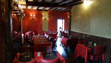 L’intérieur d’un restaurant présente des chaises à revêtement rouge, des tables dressées avec des verres à vin et des luminaires fixés au mur.