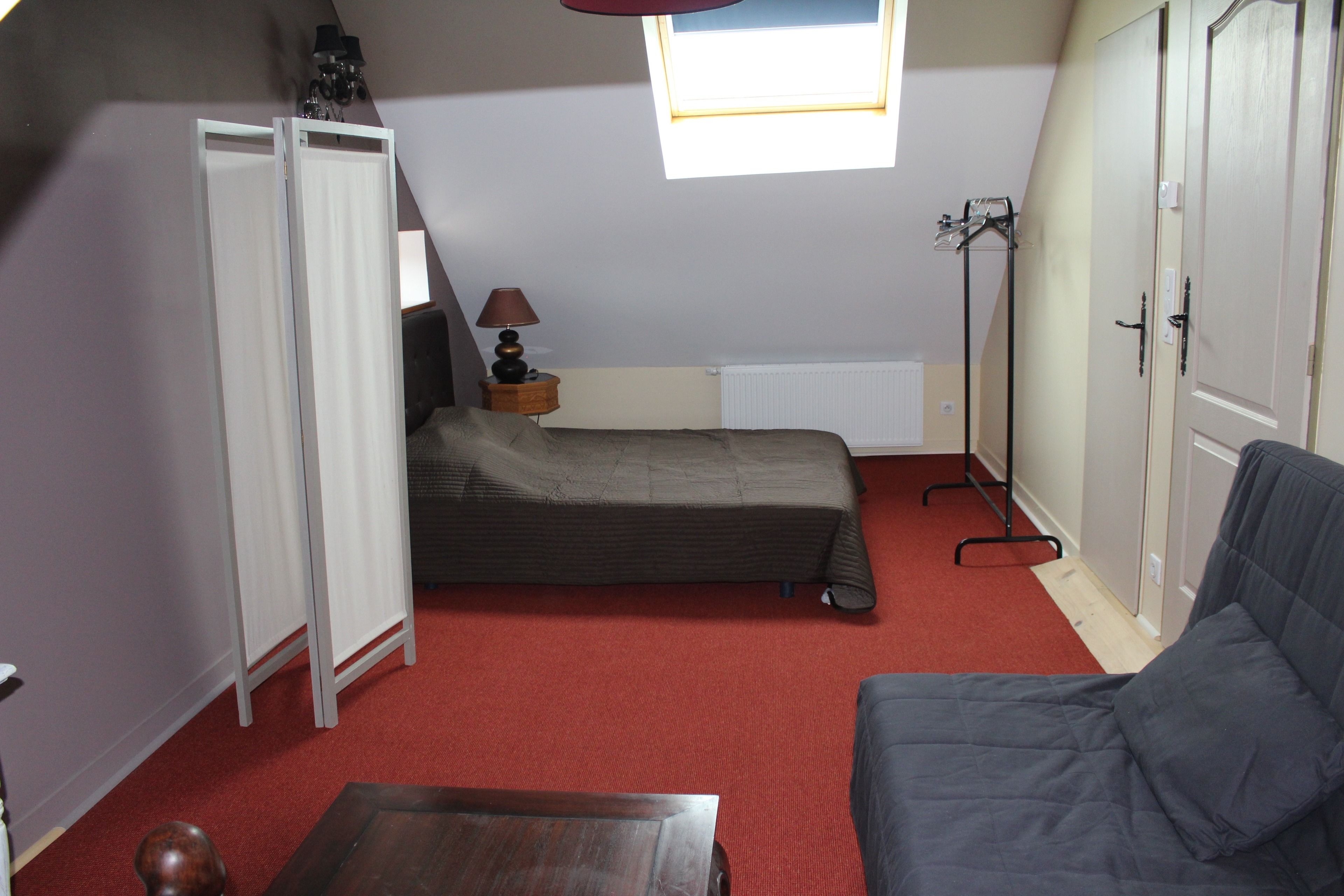 A small, compact room with a bed, a sofa, a table, and a wardrobe.