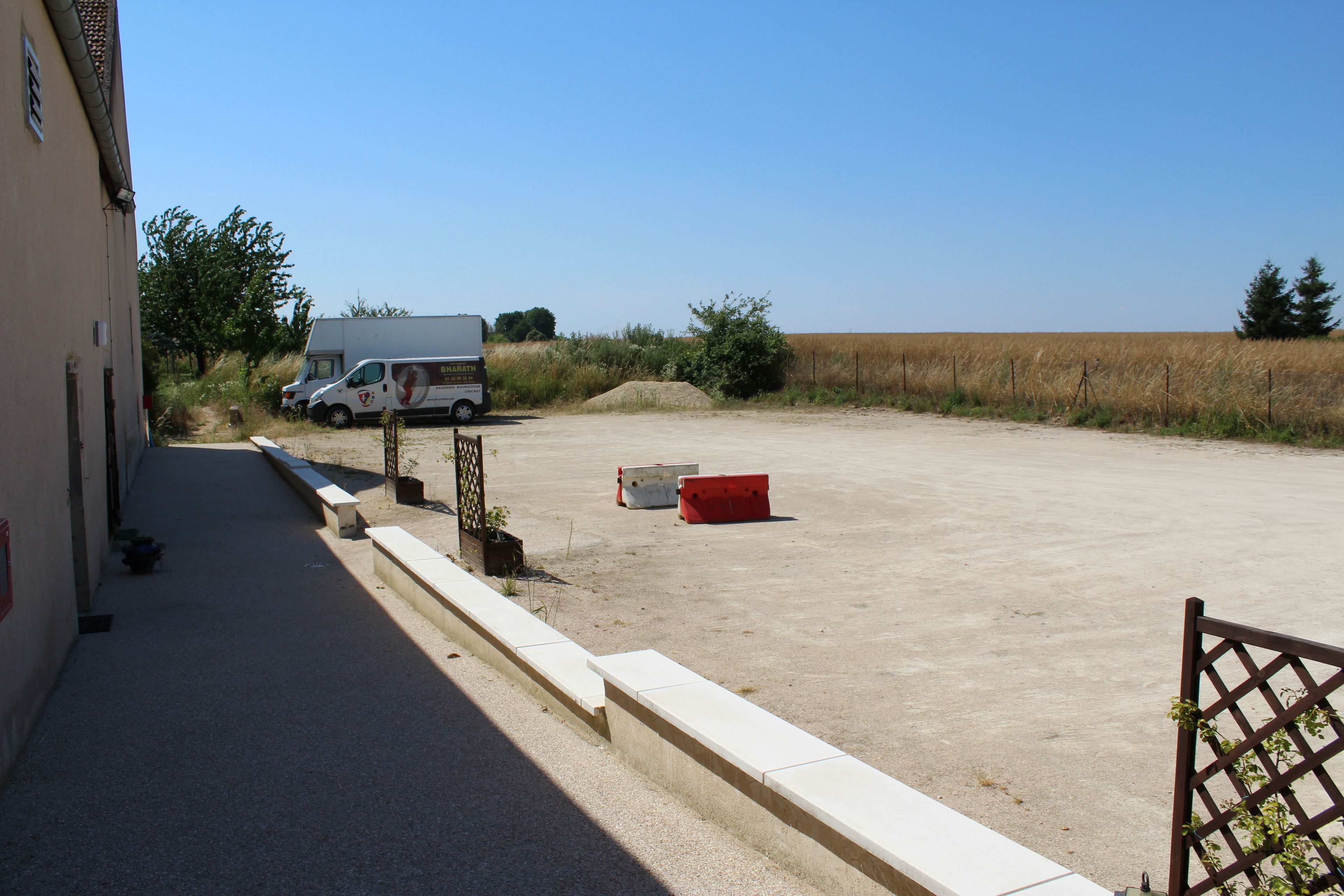 A parking area with a white van, a red container, and a building with a sloped roof.