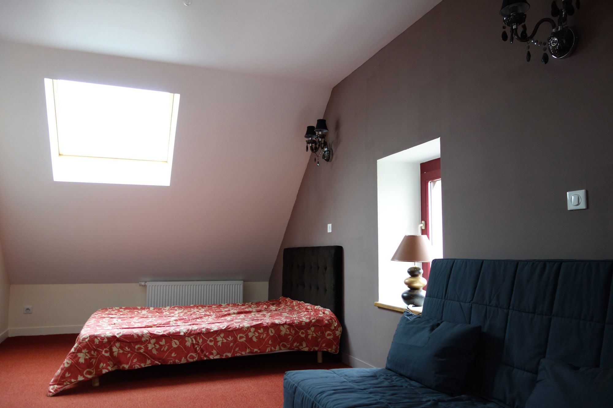 Une chambre à coucher avec un lit, un canapé bleu, une fenêtre, un radiateur et un miroir.