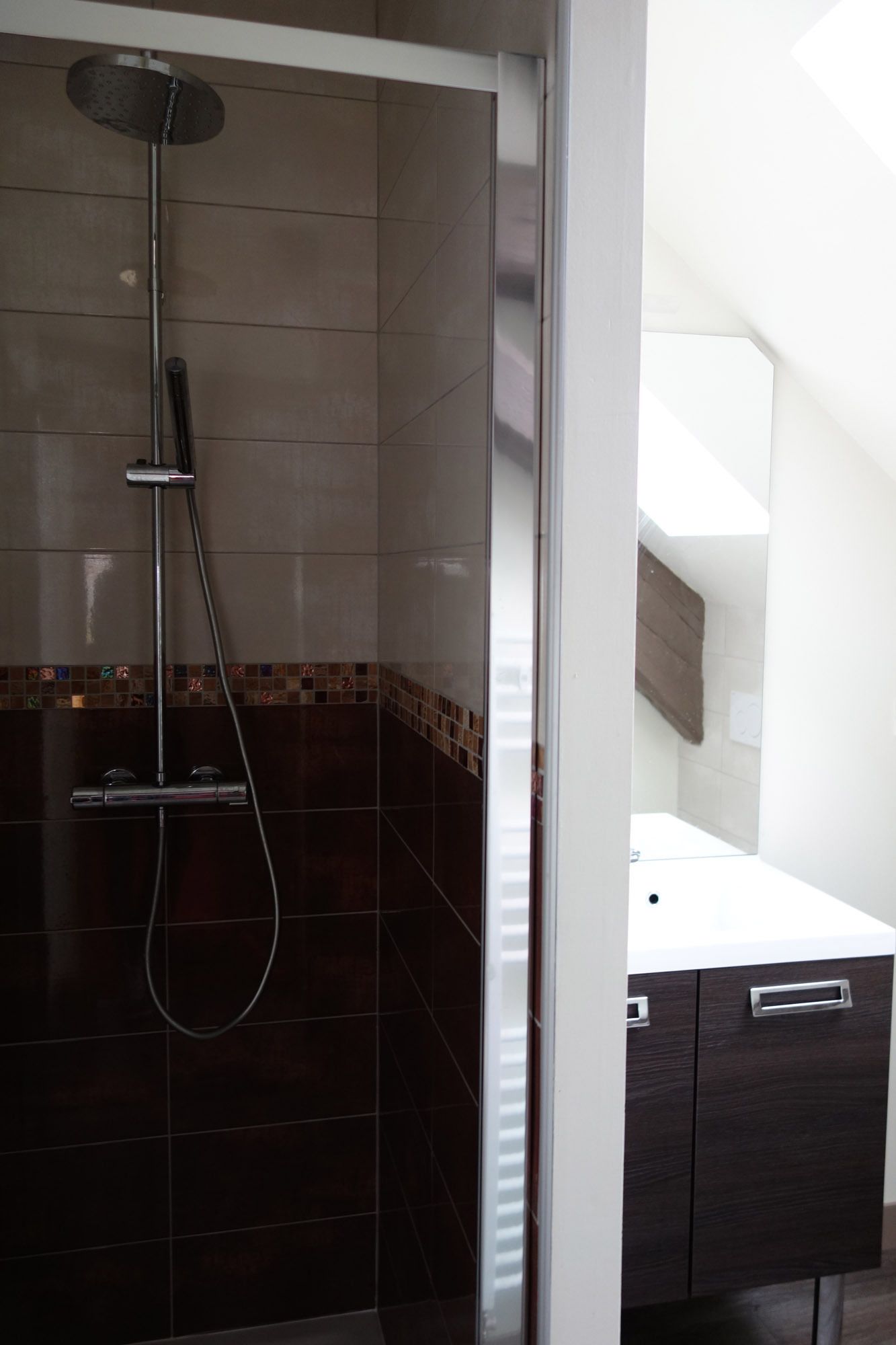 Un baño moderno con ducha, baldosas oscuras y encimera blanca.