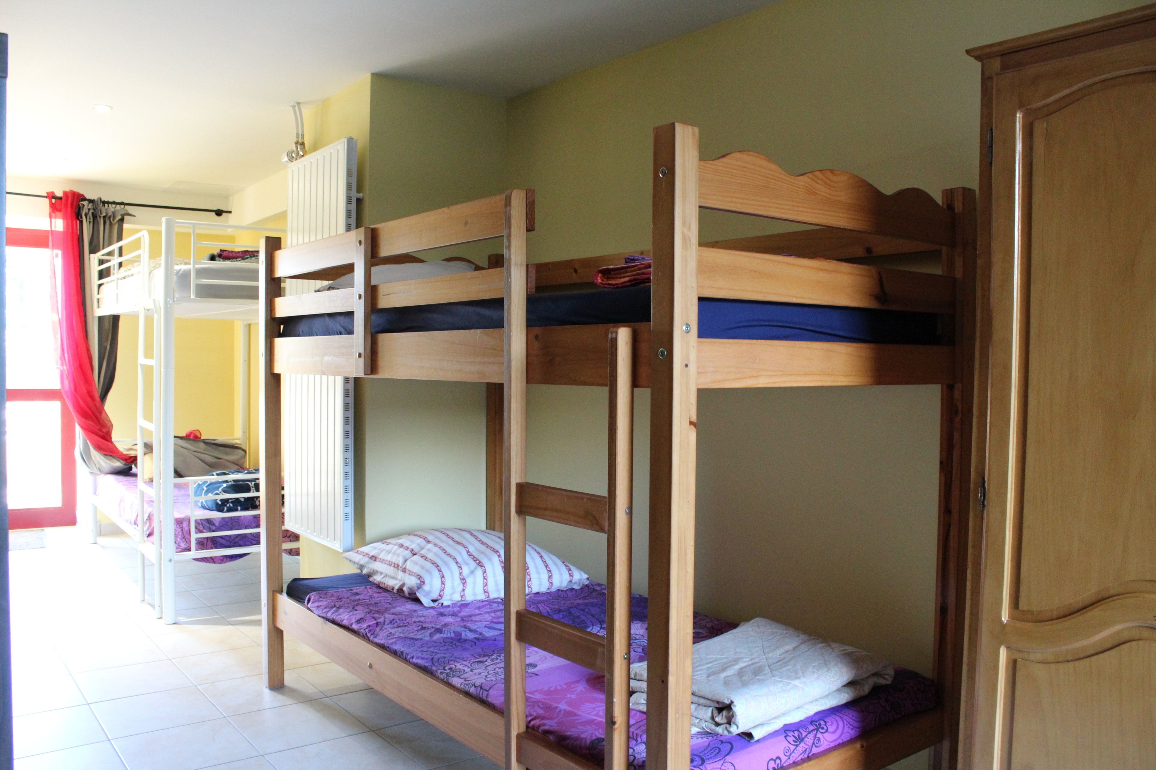 A bunk bed room with a wooden wardrobe and a red curtain.