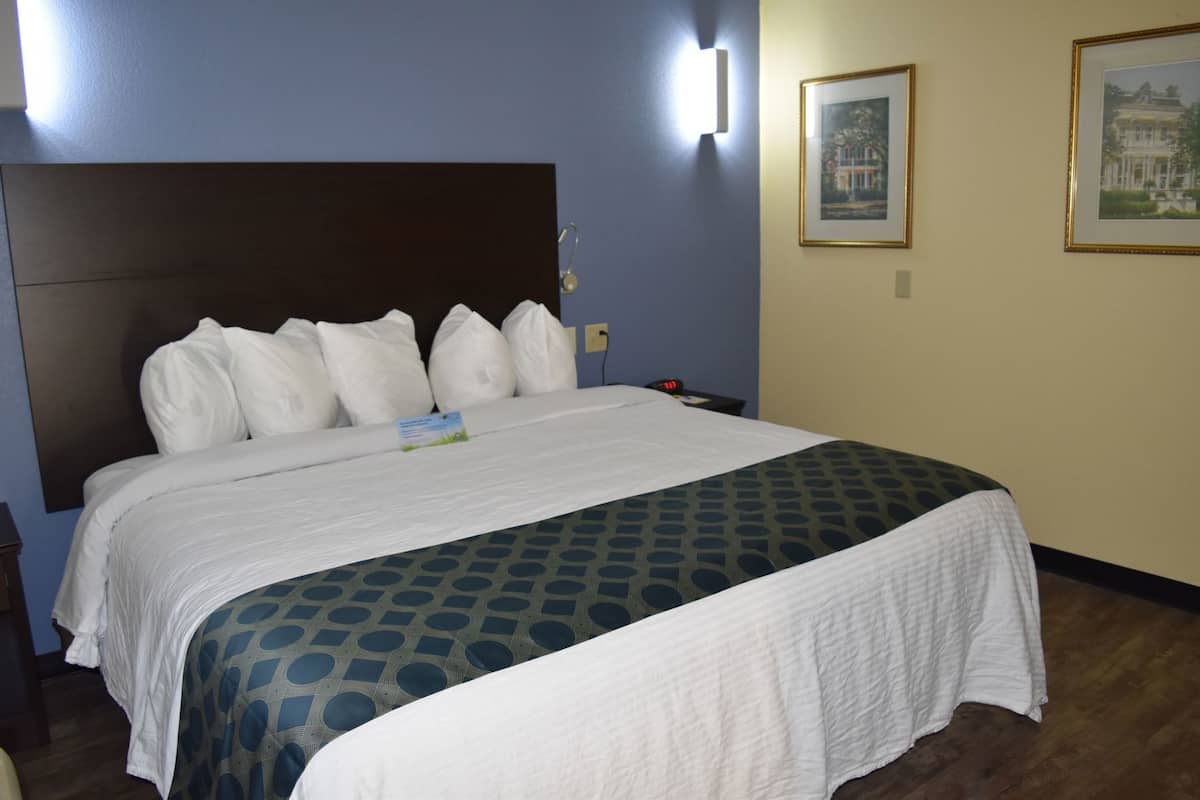 A hotel room with a large bed, a headboard, a nightstand, a wall clock, and framed pictures on the wall.