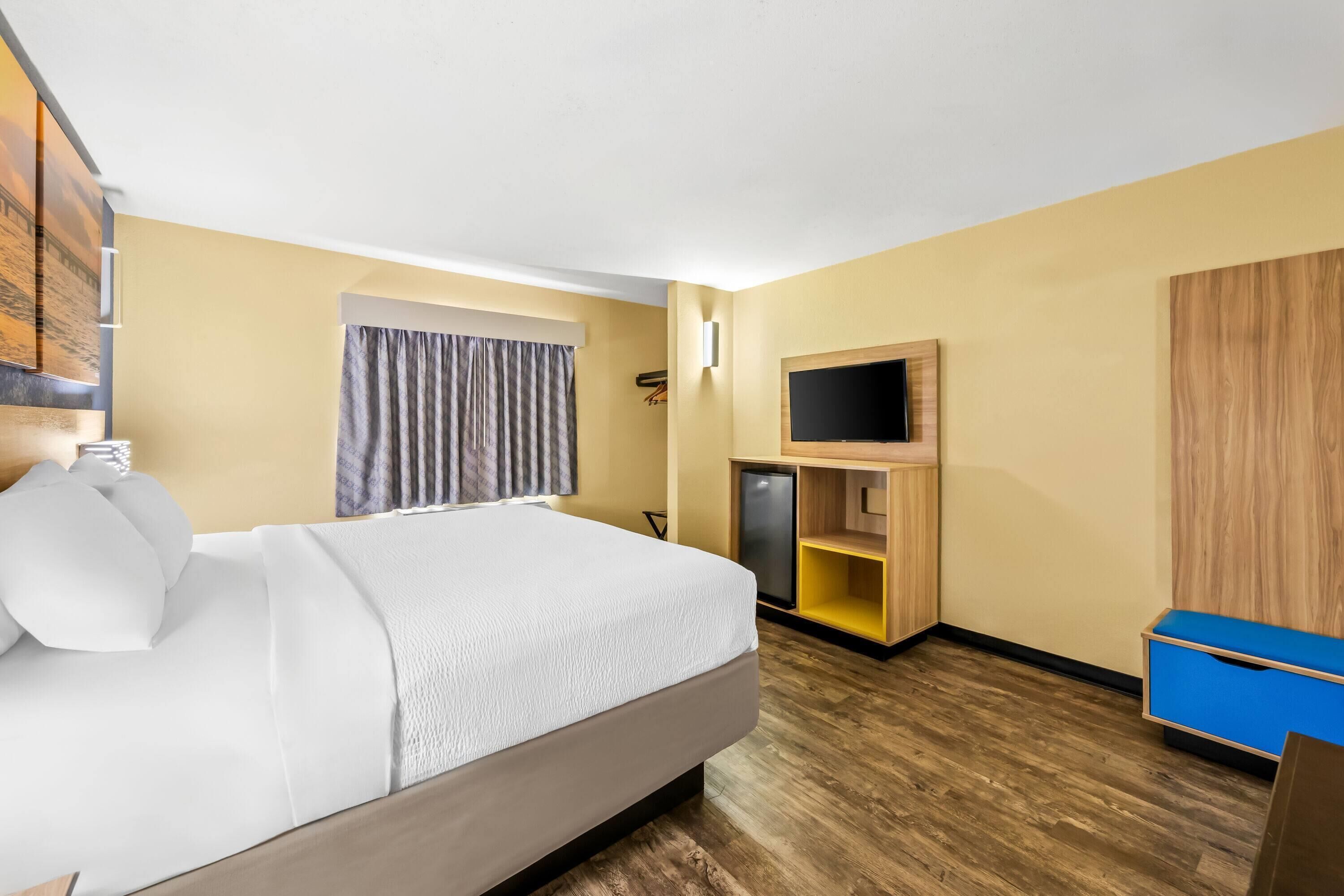 Une chambre d’hôtel équipée d’un lit, d’une télévision, d’un mini-réfrigérateur, d’une armoire et d’un bureau.