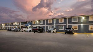 A hotel with a row of rooms, a parking lot with several cars, and a sunset sky. - Days Inn by Wyndham New Orleans Pontchartrain (New Orleans)
