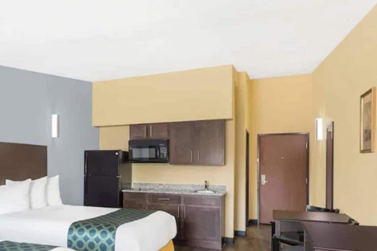 A hotel room with a bed, a kitchenette, a flat-screen TV, and a door.